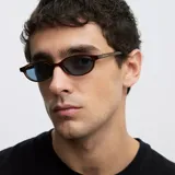 Lentes de sol con montura ovalada de acetato en color mostaza y cristales polarizados en tono celeste.