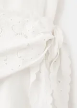 Vestido midi color blanco con diseño evasé, cuello redondo y sin mangas de tirante ancho. Cuenta con un detalle de pañuelo bordado en la cintura con cierre de cremallera lateral.