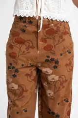 Jean de corte baggy con diseño de tiro medio y estampado floral en tonos tierra sobre base marrón. Confeccionado en algodón peinado de alta resistencia.