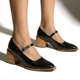 Zapato tipo Mary Jane de cuero vacuno con textura grabada, color negro. Presenta una tira con hebilla metálica sobre el empeine, punta cuadrada y taco bloque de madera natural.