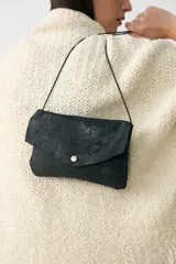 Bandolera pequeña de cuero negro con acabado laminado, diseño tipo sobre con cierre de broche a presión y correa de cuero fina extraíble.