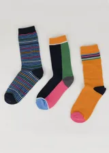 Pack de tres pares de medias de media caña con diseños variados: un par a rayas horizontales de colores sobre fondo azul marino, un par con bloques de color negro, verde y rosa, y un par color naranja con rayas horizontales en la parte superior.
