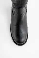 Bota de caña alta confeccionada en cuero legítimo negro, con diseño de textura granulada en la parte superior y acabado liso en la puntera. Cuenta con un taco bajo y suela plana.