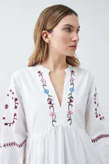 Vestido midi blanco con bordados de flores en el escote, mangas y ruedo.