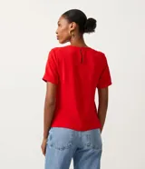 Blusa blanca de poliéster con cuello redondo, mangas cortas, cierre trasero en forma de gota, pequeñas aberturas laterales y acabados en pespuntes en las mangas y el cuello.