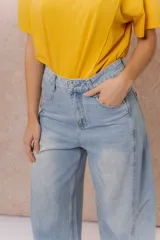 Pantalón de jean estilo barrel con tiro alto y pierna amplia de diseño curvo. Presenta un lavado celeste claro con efecto desgastado, cierre y botón frontal, y bolsillos funcionales.