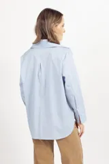 Camisa de corte clásico y diseño holgado, color celeste, con cuello camisero, cierre frontal de botones y mangas largas con puños abotonados.