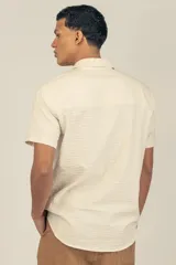 Camisa de manga corta color crema con textura, botones de madera y parche con logo.