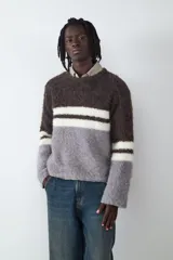 Sweater de cuello redondo con diseño de bloques de color en tonos marrón, gris y blanco, con textura de tejido de punto esponjoso y mangas largas.