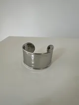 Brazalete rígido tipo cuff de acero quirúrgico con acabado plateado y superficie de textura irregular.