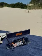 Necessaire de diseño rectangular, confeccionado en una combinación de cuero azul marino y material vinílico transparente. Cuenta con cierre superior, correa de muñeca desmontable y una etiqueta de cuero con el logo de la marca grabado en el frente.