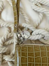 Billetera pequeña de cuero con textura de reptil, color verde pistacho. Cuenta con cierre metálico perimetral, correa de muñeca extraíble y detalle de moneda metálica plateada con logo grabado.