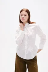 Camisa blanca de poliéster con cuello clásico, manga larga con puños anchos y detalle de frunces en la cintura que crea un efecto entallado.