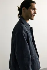 Sobrecamisa regular fit confeccionada en tejido de algodón negro con estructura canvas. Tiene cuello solapa, manga larga con puño abotonado, bolsillos de plastrón con solapa en la cadera y un bolsillo en el pecho. Cierre frontal con botones ocultos bajo solapa.