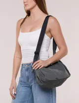 Cartera bandolera de lona naranja en forma de medialuna, con correa ajustable negra y cierre principal.