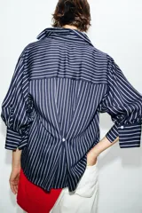 Camisa de corte oversize con estampado de rayas verticales, cuello solapa, escote en pico y mangas abullonadas con puños anchos. Cierre frontal mediante botones.
