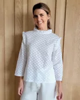 Blusa blanca con cuello alto con volados y mangas 3/4 con volados en los hombros.