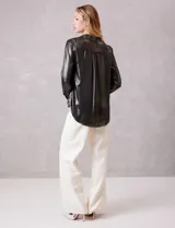 Camisa de manga larga con acabado satinado y efecto metalizado en color gris oscuro. Presenta cuello camisero clásico, cierre frontal con botones forrados y puños estructurados.