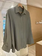 Camisa oversize color verde militar con finas rayas verticales de lurex, cuello camisero y mangas largas con puños anchos.