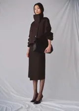 Chaqueta marrón de corte recto y diseño crop, confeccionada en mezcla de algodón y poliamida con forro interior de poliéster. Presenta cuello alto tipo embudo, doble botonadura frontal, manga larga y dos bolsillos laterales.