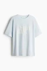 Remera de algodón color celeste claro, corte holgado, con cuello redondo y manga corta. Presenta un estampado frontal con la palabra "Sunday." en color blanco.