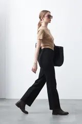 Pantalón de fit recto color beige, confeccionado en cotton spandex. Presenta costuras visibles y bordados decorativos en tono dorado/marrón claro. El ruedo del pantalón tiene un borde festoneado.