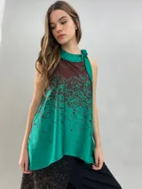 Blusa de satén con escote halter y cuello elevado anudado lateralmente. Presenta un diseño estampado degradado en tonos verde esmeralda y azul, con corte holgado y caída fluida.