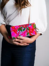 Billetera de tela rectangular con cierre perimetral, bordado artesanal multicolor de flores y aves sobre fondo lila, y tirador con pompón y cuentas de madera.