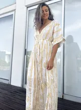 Túnica larga de estilo bohemio, color blanco con estampado de arabescos en tono dorado. Presenta escote en V profundo, mangas amplias tipo kimono y ajuste elástico en la cintura con cordón decorativo terminado en borla.
