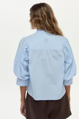 Camisa blanca de cuello mao con volados, mangas abullonadas y cierre frontal con botones.