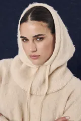 Capucha de tejido de punto suave en color beige, con diseño envolvente que cubre la cabeza y el cuello, cuello amplio y cordón de ajuste frontal.