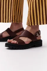 Sandalia de cuero sintético color camel, con plataforma track y hebilla metálica.