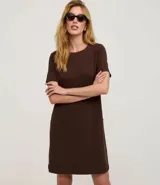 Vestido corto marrón oscuro, estilo camiseta, con escote redondo, mangas cortas y bolsillos laterales. El bajo es redondeado.