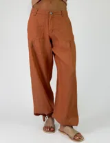 Pantalón de lino color beige, de corte holgado tipo jogger con puños ajustables con cintas en los tobillos, bolsillos laterales y cierre frontal con botón y cremallera.