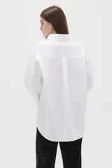 Camisa blanca de algodón, de corte holgado, manga larga con puños anchos y cuello camisero. Cuenta con cierre frontal parcial de botones.