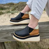 Zapatos de cuero color negro con paneles laterales en marrón y talón en marfil, con suela track alta y gruesa en tonos blanco y tostado.