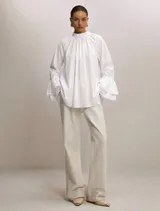 Blusa blanca de algodón con cuello alto fruncido, corte amplio y mangas largas terminadas en doble volado.