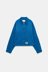 Chaqueta de cuello solapa y manga larga, de color azul, con bolsillos de vivo en los laterales, detalle de pliegues en la espalda y cierre frontal con cremallera. Cuenta con una etiqueta con logo bordado en el bajo.