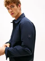 Campera azul marino de tejido técnico de Tommy Hilfiger, con cierre frontal de cremallera, cuello camisero, bolsillos laterales y parche engomado en la manga.