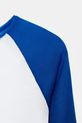 Camiseta de manga larga con cuerpo blanco y mangas raglán azules. Tiene cuello redondo y corte slim fit.