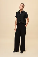 Pantalón negro de pierna ancha y calce fluido, con pinzas delanteras y bolsillos laterales.