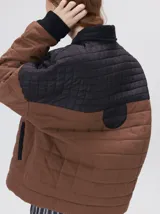 Campera acolchada con diseño de bloques de color en tonos terracota y beige. Presenta cuello camisero y puños en pana negra, cierre frontal oculto con botones a presión y costuras capitoneadas en toda la prenda.