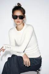 Jersey Zara de punto liso color negro, con cuello redondo, manga larga y detalle de botones dorados en los puños.