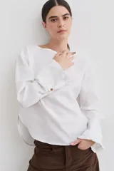 Blusa de lino con cuello bote y mangas largas terminadas en puños acampanados con volados. Presenta un cierre con botón en la espalda.