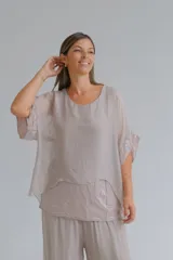 Blusa de diseño holgado en color beige, compuesta por una capa superior de tela semitransparente y una capa inferior con detalle de lentejuelas. Presenta mangas cortas con bordes decorados con lentejuelas y cuello redondo.