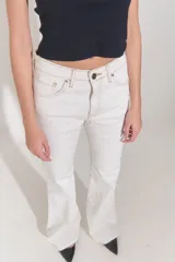 Jean de corte oxford y tiro bajo, confeccionado en denim blanco. Presenta diseño de cinco bolsillos, cierre frontal con cremallera y botón metálico, y costuras a contratono.