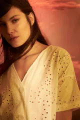 Blusa blanca con bordado inglés, escote en V, manga corta y cierre frontal con botones.