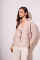 Blusa color visón con escote en V profundo y lazos ajustables en el frente, mangas largas y corte holgado.