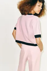 Chaqueta de punto rosa con ribetes negros en el cuello, la botonera, los bolsillos, los puños y el ruedo. Cuenta con manga corta, cuello redondo, bolsillos frontales de plastrón con botones y cierre frontal abotonado.