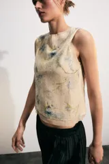 Top corto sin mangas, con cuello redondo, confeccionado en tejido de punto cubierto de lentejuelas con estampado floral en tonos azules y verdes sobre fondo beige. Cuenta con cierre en la espalda con abertura y botón.